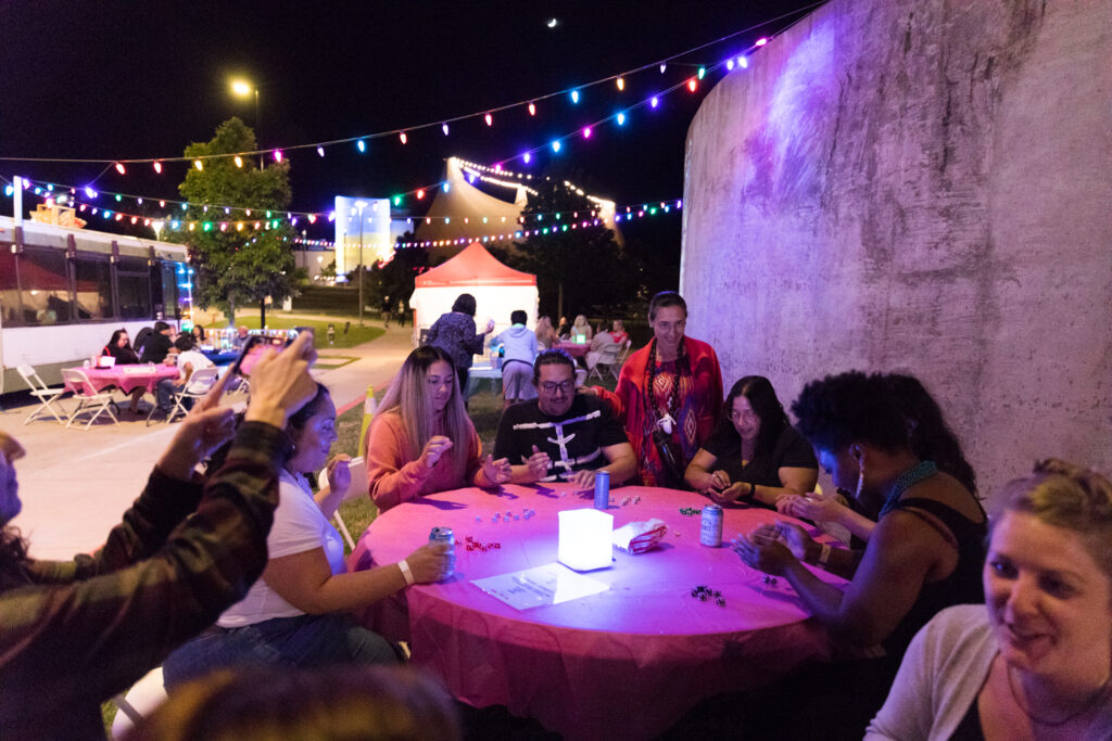 A group of happy people play games at night under string lights.
